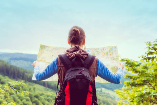 Woman traveler with backpack checks map to find directions in wilderness area, real explorer. Travel Concept stock photo