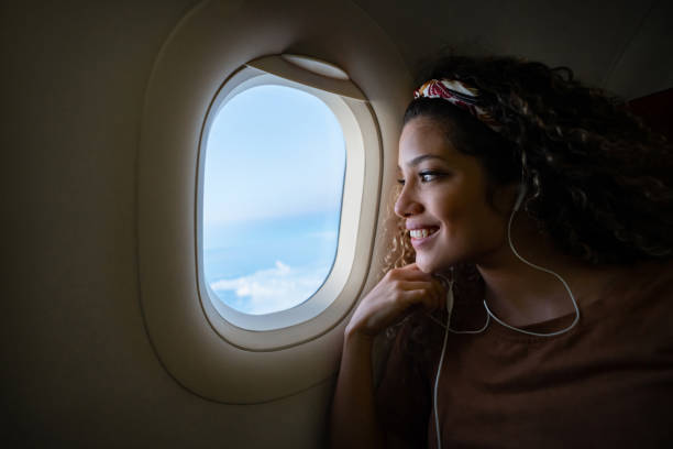 Portrait of a happy woman traveling by plane and listening to music with headphones while looking through the window - lifestyle concepts