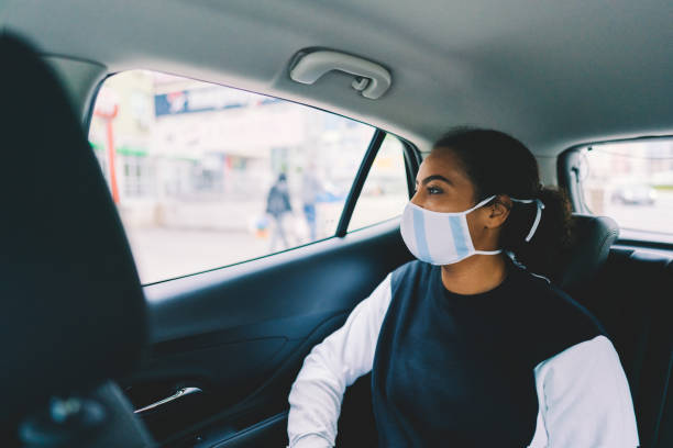 Woman traveling by taxi during COVID-19 pandemic Mixed race woman with protective face mask travel by taxi back seat stock pictures, royalty-free photos & images