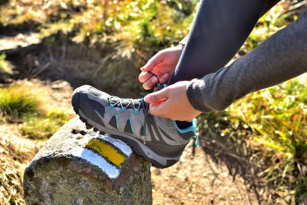 Woman tying her trekking shoes on a hiking stone marking the tourist route stock photo