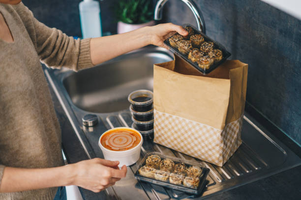 Woman unpacking takeaway food delivery Woman carefully unpacking take out food boxes near the kitchen sink take out food stock pictures, royalty-free photos & images