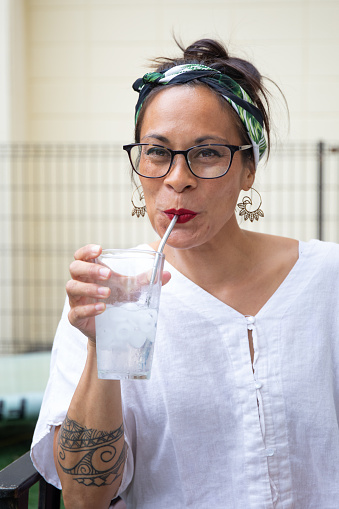 A mixed race woman drinking from a metal reusable straw instead of plastic straws to help save on waste for the environment.