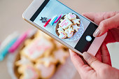 女性がスマート フォンを使用して新鮮な装飾が施されたクッキーの写真を撮る
