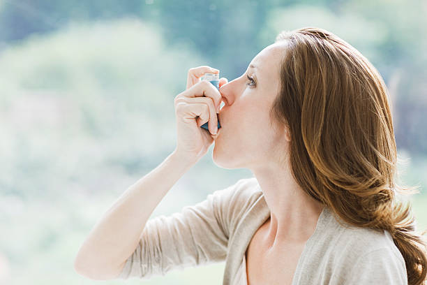 woman using asthma inhaler - astmatisch stockfoto's en -beelden