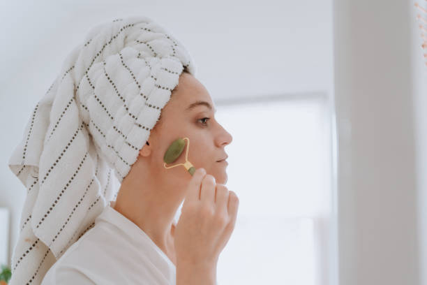 Woman using jade roller on her face at home stock photo