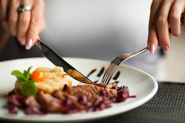 Woman using knife and fork to cut her dinner stock photo
