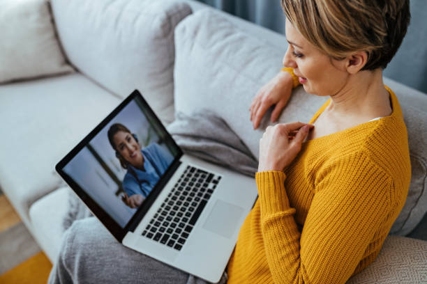 Woman using laptop and having video call with her doctor while sitting at home. Young woman sitting on the sofa while talking with her doctor over a laptop. severe acute respiratory syndrome photos stock pictures, royalty-free photos & images