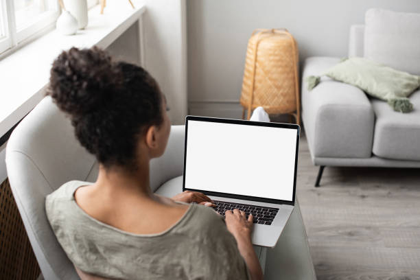 Woman using laptop computer on sofa, white blank empty screen mock-up stock photo