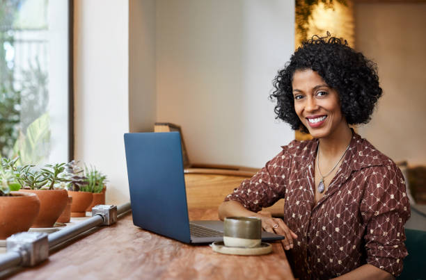 Woman using laptop while sitting in coffee shop Portrait of smiling woman with laptop sitting in coffee shop. Young female with curly hair in cafe. She is in casuals. 35 39 years stock pictures, royalty-free photos & images