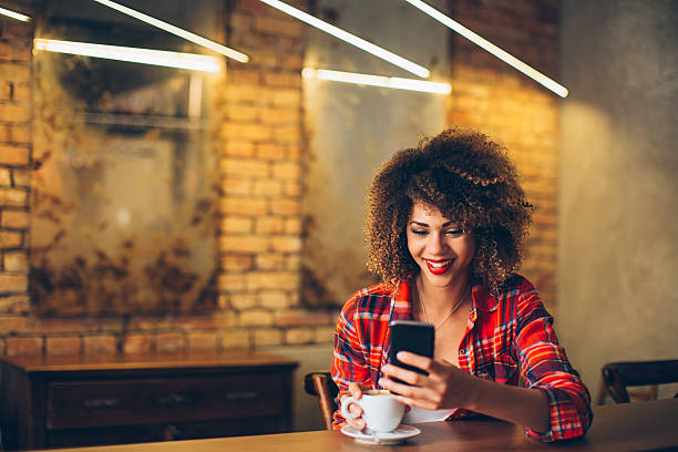 Woman using mobile phone Young woman at cafe drinking coffee and using mobile phone curley cup stock pictures, royalty-free photos & images