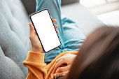istock Woman using mobile smartphone with blank white screen on a sofa in living room. 1272379051