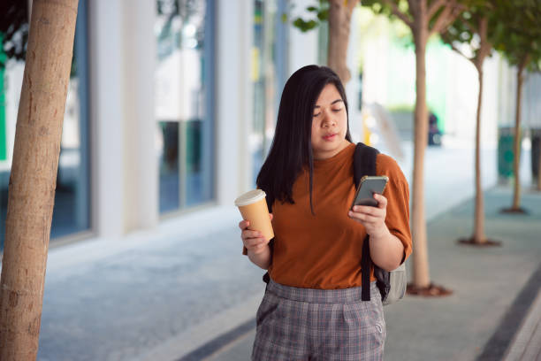 Woman using phone in the street on coffee break, carrying coffee to go stock photo