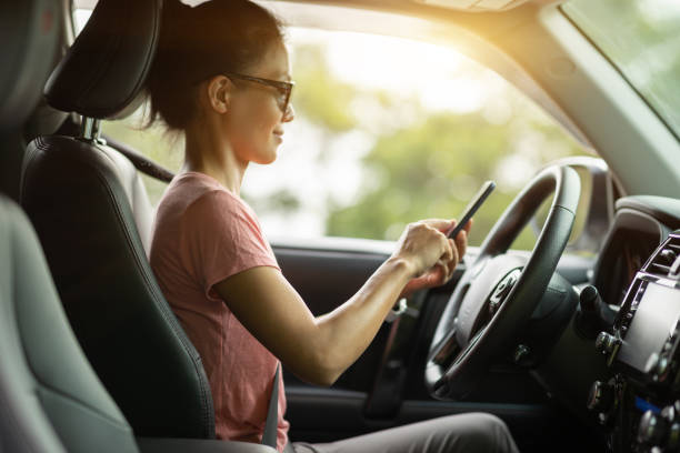 Woman using smartphone driving car on sunrise mountain road stock photo