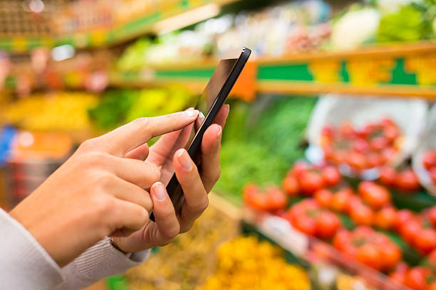 Woman using smartphone near vegetable stand stock photo