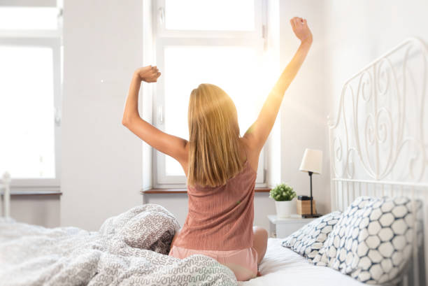 Woman wakes up at sunrise Back view of woman stretching in bed. Wake up at sunrise waking up stock pictures, royalty-free photos & images