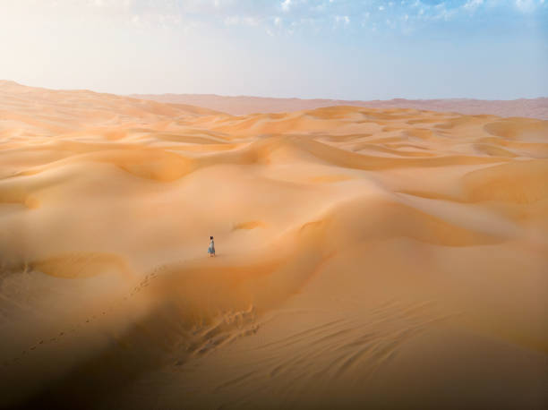 Woman walking on the desert sand dunes aerial view Woman walking on the desert sand dunes aerial view at sunset hot arab woman stock pictures, royalty-free photos & images