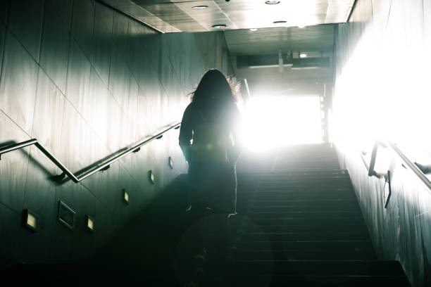 woman walking to light in dark stairs - stairs subway imagens e fotografias de stock
