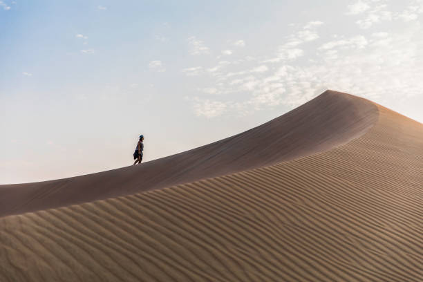 woman walking to the top of a dune in the desert woman walking to the top of a dune in the middle of the desert and clouds hot peruvian women stock pictures, royalty-free photos & images