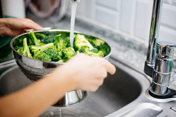 woman washing broccoli in the kitchen sink - woman chopping vegetables imagens e fotografias de stock