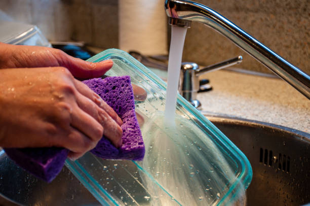 Woman Washing Dishes Woman washing a plastic food storage container with a sponge in kitchen sink. plastic container stock pictures, royalty-free photos & images