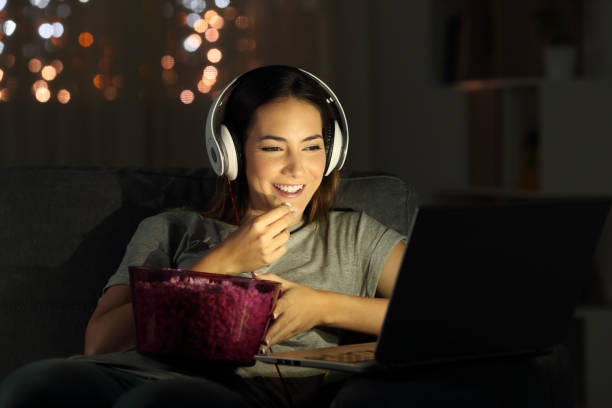 Woman watching online tv in the night Single woman watching online tv in the night sitting on a couch in the living room at home part of a series stock pictures, royalty-free photos & images