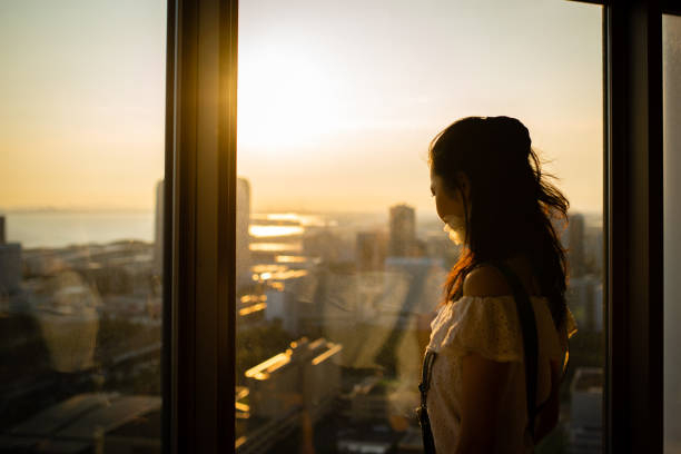 donna che guarda il tramonto dalla finestra dell'appartamento - guardare fuori dalla finestra foto e immagini stock