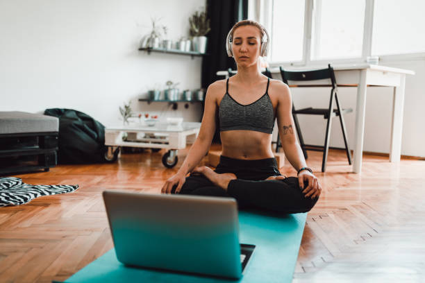 Woman watching tutorial on laptop and doing yoga at home stock photo