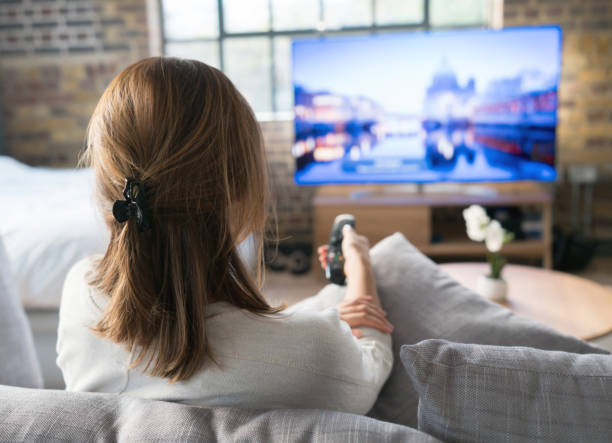 Woman watching tv at home Woman relaxing at home watching tv and holding the remote control watching tv stock pictures, royalty-free photos & images
