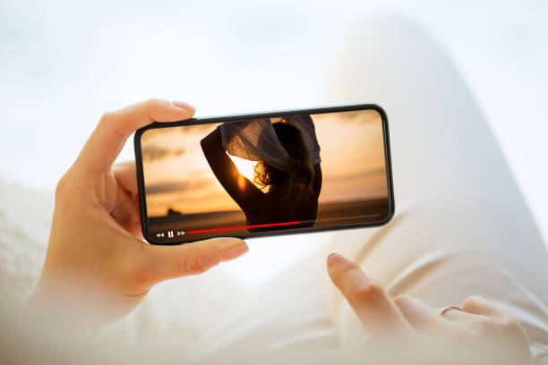 携帯電話でビデオを見ている女性 - 横位置 ストックフォトと画像