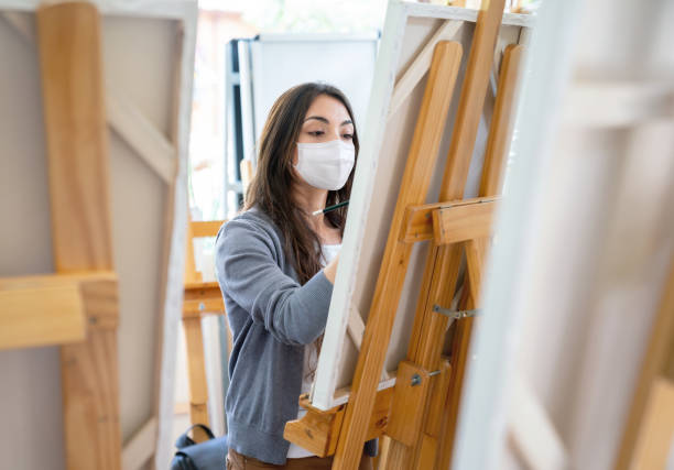 woman wearing a facemask while painting in an art class - sala de aula universidade arte imagens e fotografias de stock