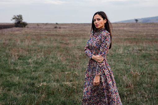 Portrait of a beautiful young woman wearing a long floral pattern dress on a lovely autumn day in nature