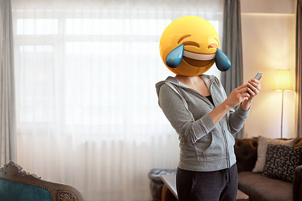 Woman wearing emoji masks while looking at her phone. Woman wearing tears of joy emoji masks while looking at her phone. Image created by mix of photography and CGI. laughing emoji stock pictures, royalty-free photos & images