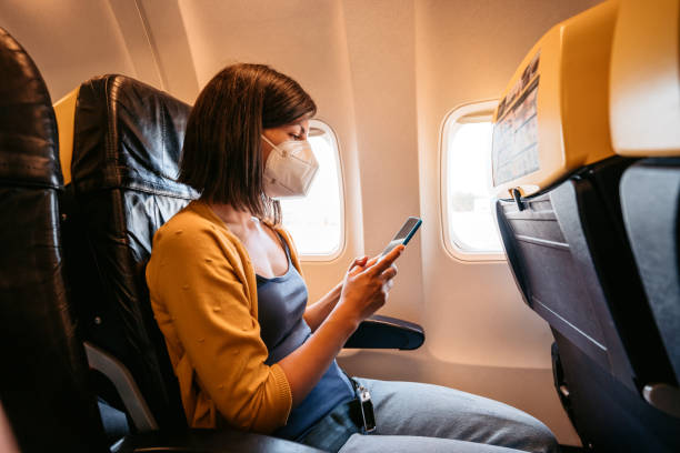 Woman wearing face mask is using smartphone in airplane stock photo