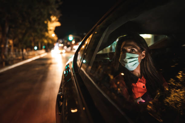 donna che indossa la maschera facciale seduta sul sedile posteriore e guardando attraverso il finestrino - taxi foto e immagini stock