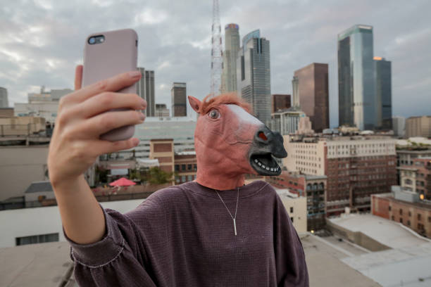 Woman wearing horse mask taking selfie on downtown roof Funny photo of woman wearing horse head mask taking selfie on roof in downtown Los Angeles. horse mask photos stock pictures, royalty-free photos & images