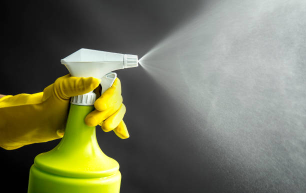 Woman wearing yellow rubber gloves using green spray bottle and spraying liquid mist in air, cool lighting effect. Lot of copy space.  cleaning product stock pictures, royalty-free photos & images