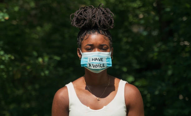 Woman wears face mask with protest message A young woman wears a face mask during global pandemic that says "I have a voice." protestor stock pictures, royalty-free photos & images