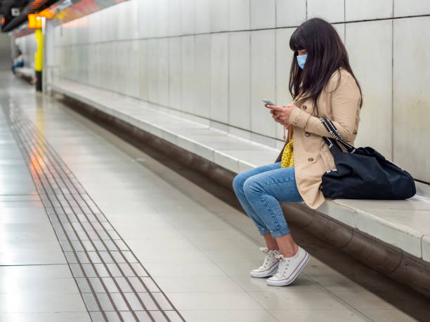 Woman with a face mask sitting in a subway station with cellphone stock photo