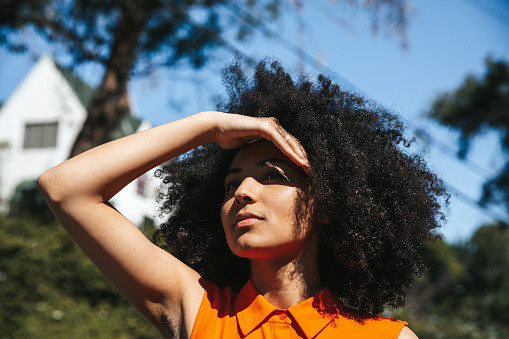 Woman with afro hair covering her eyes from the sun.