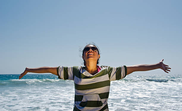 Woman with arms stretched looking at sky at the beach stock photo