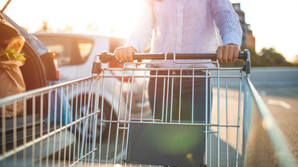 Woman with bags and shopping cart loads a car. Woman with bags and shopping cart loads a car. Woman putting bags into car after shopping. Woman pushing supermarket cart in urban public parking cart stock pictures, royalty-free photos & images