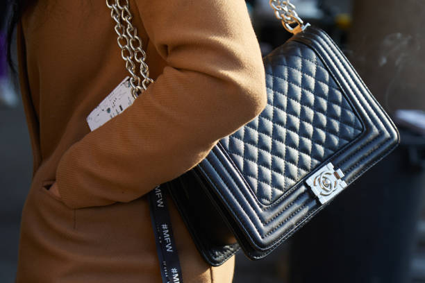 Woman with black Chanel leather bag with silver chain and beige coat MILAN - JANUARY 14: Woman with black Chanel leather bag with silver chain and beige coat before MSGM fashion show, Milan Fashion Week street style on January 14, 2018 in Milan. brand name stock pictures, royalty-free photos & images