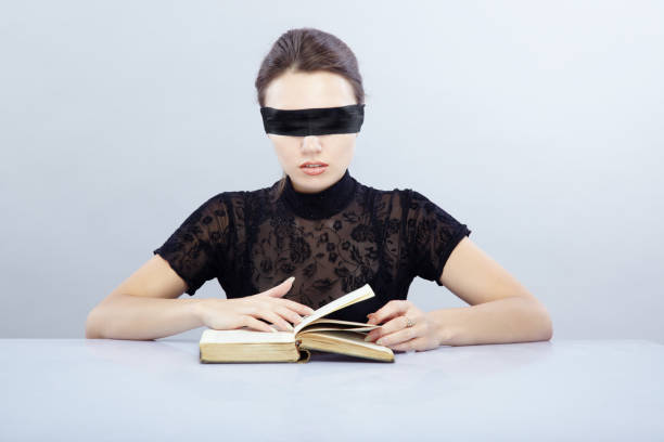 Woman with blindfold trying comprehend textbook. Conceptual symbol of incomprehensible subject stock photo