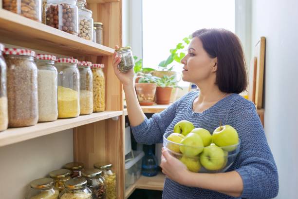 Woman with bowl of green apples in pantry, organizing in kitchen Woman with bowl of green apples in pantry near wooden shelving with jars containers, storing cereals food, organizing in the kitchen pantry stock pictures, royalty-free photos & images