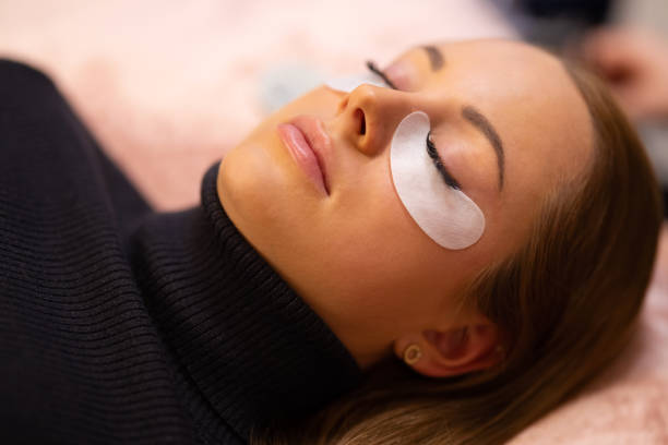 Woman With Cotton Pads Lying During Eyelash Extension Treatment stock photo