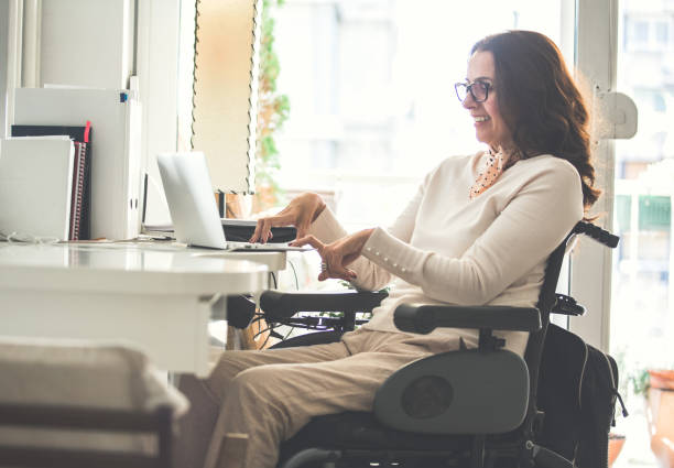 Woman with disability working Side view of a happy woman with physical disability working on a laptop in the office. wheelchair stock pictures, royalty-free photos & images