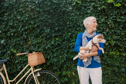 Beautiful mature woman holding dog, leaves behind them and bicycle
