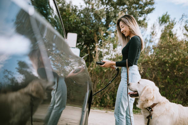 woman with dog plugs in electric vehicle to charge - electric car imagens e fotografias de stock