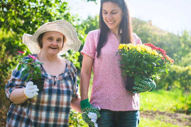 Woman with Down Syndrome and her relative planting flowers together. Gardening. stock photo
