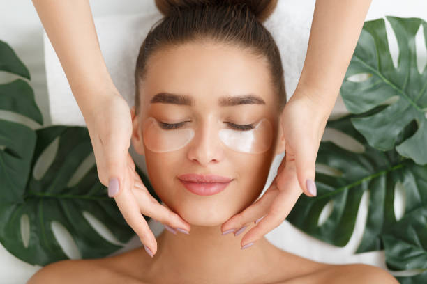 vrouw met eye patches met gezicht massage - schoonhedisalon stockfoto's en -beelden